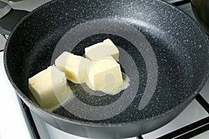 Woman cooking melting butter on frying pan mixing with wooden spatula.