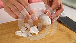 Woman cooking peeling garlic using knife on wooden board, hands close-up.