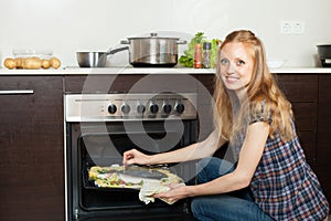 Woman cooking saltwater fish in oven at kitchen