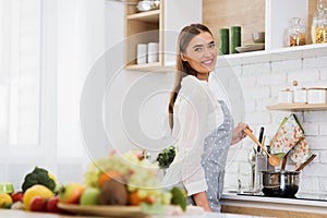 Woman cooking in saucepan, stiring soup with wooden spoon