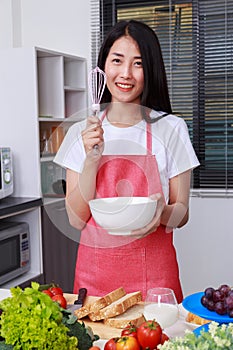 Woman cooking and whisking eggs in a bowl in kitchen room