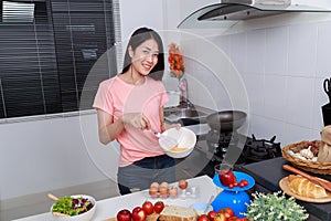 Woman cooking and whisking eggs in a bowl in kitchen