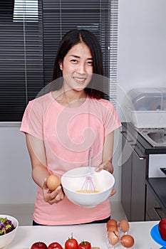 Woman cooking and whisking eggs in a bowl in kitchen
