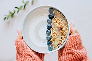 Woman in coral woolen sweater eating breakfast bowl with muesli and yogurt, berries and hazelnuts. Clean eating, vegetarian, vegan