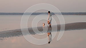 Woman and corgi dog walk together on sea beach while traveling outside.