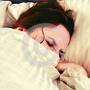 A woman with a coronavirus is covered with a blanket and squints while lying on the bed