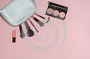 Woman cosmetic bag, make up beauty products on pink background. Makeup brushes, pink lipstick and rouge palettes. Decorative cosme