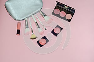 Woman cosmetic bag, make up beauty products on pink background. Makeup brushes, pink lipstick and rouge palettes. Decorative cosme
