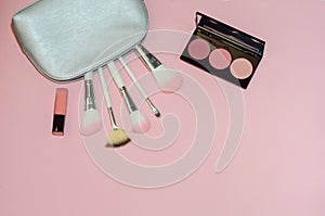 Woman cosmetic bag, make up beauty products on pink background. Makeup brushes, pink lipstick and rouge palettes. Decorative cosme