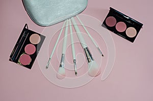 Woman cosmetic bag, make up beauty products on pink background. Makeup brushes and rouge palettes. Decorative cosmetics. Top view,