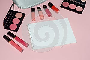 Woman cosmetic bag, make up beauty products on pink background, notebook. Red and pink lipstick. Makeup brushes and rouge palettes