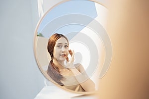 Woman with cosmetic looking at the mirror