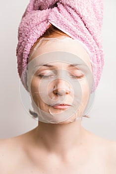 Woman with cosmetic tissue mask on face on light background