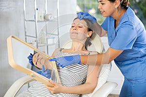 Woman cosmetologist examines patients forehead after lifting procedure and palpates forehead area