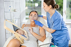 Woman cosmetologist examines patients nasolabial area after lifting procedure and palpates lips mouth