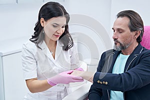 Woman cosmetologist examining male client hands before beauty procedure