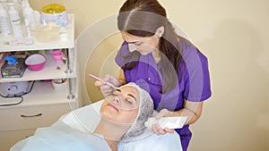 Woman cosmetologist to apply the cream-mask on the face. Cosmetic procedures