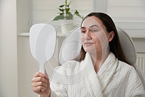 Woman in cosmetology salon satisfied with result of cosmetic procedure. Female looking at mirror and examining skin