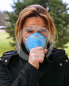 Woman coughs in sickness while wearing a blue antiviral face mask to protect from sickness.