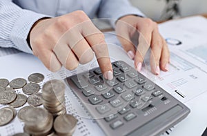 Woman counting on calculator at table with documents and coins closeup