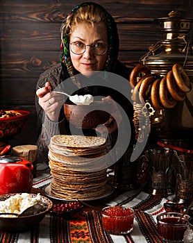 Woman in countrystyle outfit offers traitional Shrovetide Maslenitsa pancakes and treats