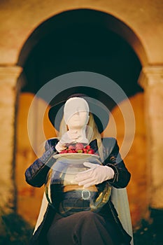 Woman covered by a mannequin head. Lady in her hands holds an aquarium with strawberries., Creative. Concept.