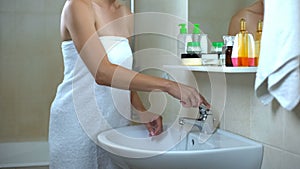 Woman covered in towel opening faucet, morning procedures, every day hygiene