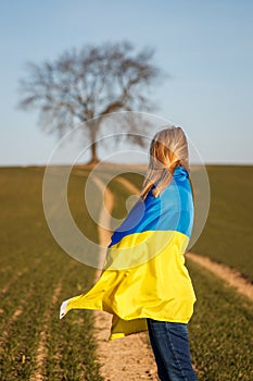 Woman covered by ukrainian flag standing in field