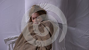 Woman covering with blanket lying in bed, feeling fever, symptoms of cold
