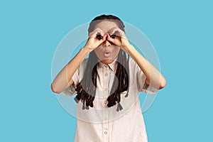 Woman covering eyes with ok signs, makes binoculars, foolishes around and looks through goggles.