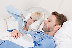 Woman Covering Her Ears With Pillow While Man Snoring