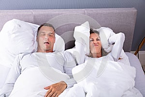 Woman Covering Her Ears With Pillow Near Snoring Man