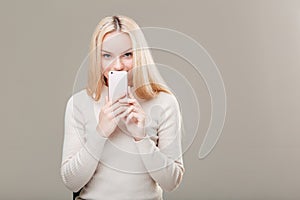Woman covering her mouth with blank smartphone screen over grey background