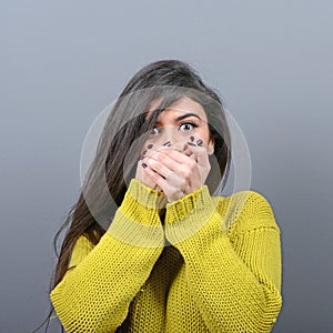 Woman covering her mouth with hands against  gray background