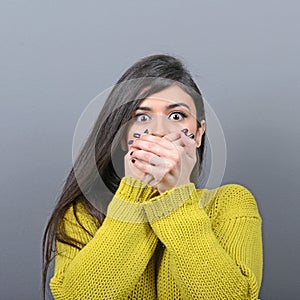 Woman covering her mouth with hands against  gray background