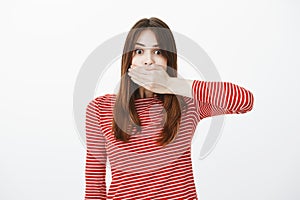 Woman covering mouth not to tell secret of friend. Studio shot of shocked and amazed caucasian female student with red
