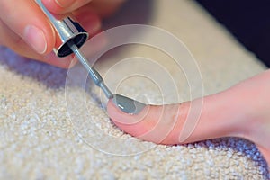 Woman is covering nails applying grey shellac gel polish at home, hands closeup.