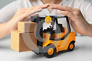 Woman covering toy forklift at white table. Logistics and wholesale concept