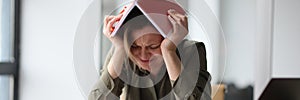 Woman covers head with book feeling tired and powerless