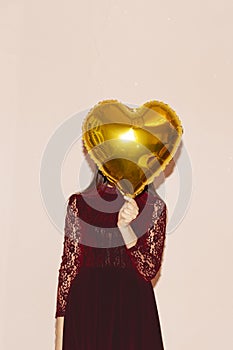 Woman covers her face with heart shaped golden air balloon. valentines day, birthday, womens day, anniversary, holiday celebration