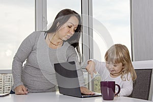 A woman covers the keyboard on a laptop with her hand from a small child. Concept: home appliances are not toys for children,