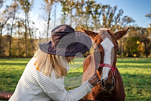 Woman with cowboy hat is talking to her young horse at farm