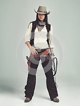 Woman, cowgirl and portrait in studio for fashion costume with confidence on grey background, weapon or outlaw. Female