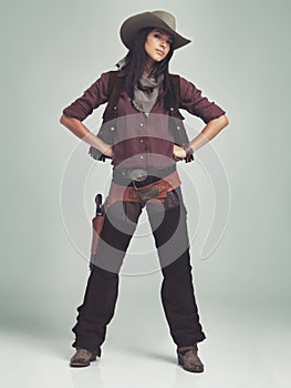 Woman, cowgirl and portrait in studio for western costume with confidence on grey background, weapon or outlaw. Female