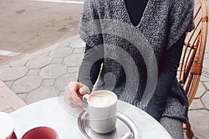 Woman in a cozy gray-blue vest spends time in street cafe