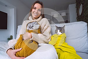 Woman in cozy sweater with her cats feeling cold and warming under a blankets