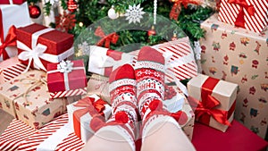 A woman, cozy and warm in a cute red socks, poses by Christmas tree, box gifts