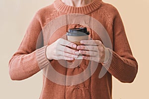 Woman in cozy warm orange sweater holding paper cup of coffee.