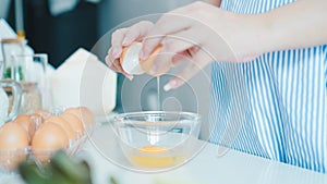 Woman cracking an egg into a bowl with standing by in kitchen.