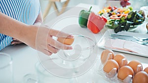 Woman cracking an egg into a bowl with standing by in kitchen.